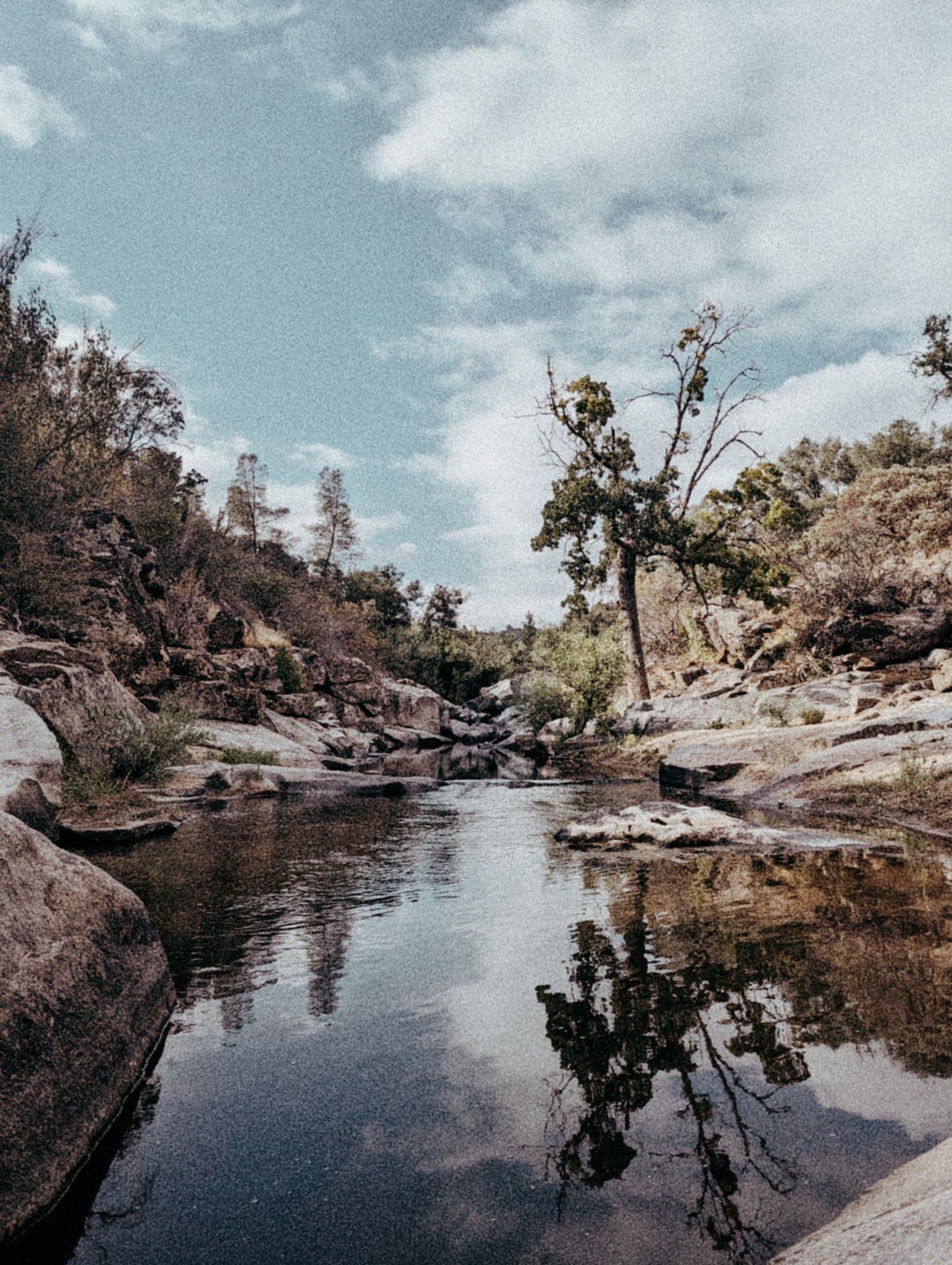 A still river pool reflecting the sky, surrounded by rocks and trees